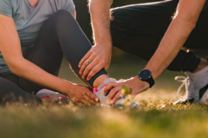man assisting his wife with ankle pain during sports training in nature
