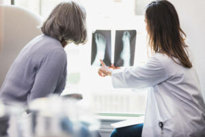A female podiatrist points out a fracture or area of concern on a female patient's foot x-ray. The patient is attentively looking at the x-ray with the doctor.