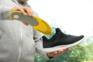 Man putting custom orthoticsinto shoe indoors, closeup. Foot care