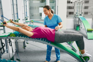 Physiotherapist assists a woman patient during spine and back rehabilitation and restores using a special rehabilitation trainer machine at rehab room