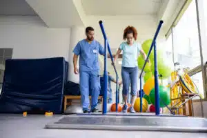A woman is undergoing physical therapy with a sports medicine physician while walking on parallel bars.