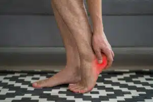 A man is suffering from foot pain due to a heel spur and plantar fasciitis while at home.