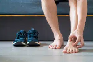 A man wearing canvas shoes scratches his legs and feet due to itchy skin caused by a fungal infection known as Athlete's Foot, originating from the athletic shoes beside him.