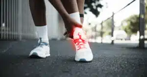 A runner experiencing ankle pain from a sprain pauses to check their feet during exercise in the city.