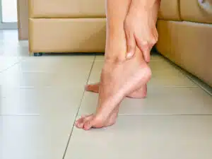 Hand resting on the ankle due to heel pain from inflammation caused by Plantar Fasciitis.